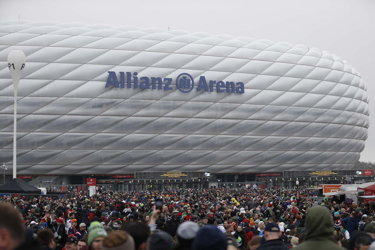 Weiße Fassade der Allianz Arena bei Tag, NFL-Fans vor dem Stadion beim Munich Game 2022
