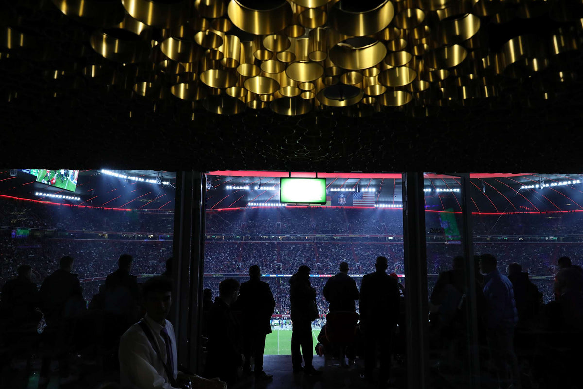 VIP-Hospitality-Bereich der Allianz Arena beim NFL Munich Game 2022: goldene Deckenleuchten, Gäste vor der Glasfront zum Spielfeld