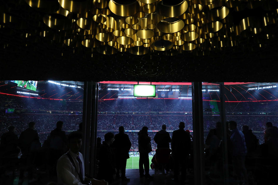 VIP hospitality area at the Allianz Arena during the 2022 NFL Munich Game: golden ceiling lights, guests by the glass wall overlooking the field